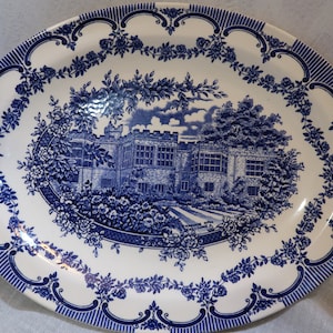 May include: A white oval ceramic serving platter with a blue and white floral border and a blue and white image of a building in the center.