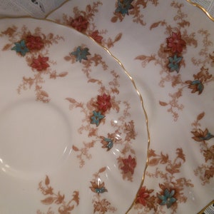 May include: Two white porcelain plates with a gold rim and a floral pattern in shades of brown, red, and blue. The plates are nested together.