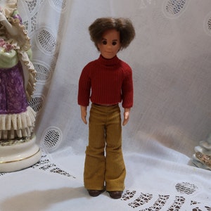 May include: A vintage doll with brown hair, wearing a red turtleneck sweater and brown corduroy pants.
