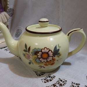 May include: A yellow teapot with a brown lid and a floral design. The teapot has a brown rim and a brown handle.