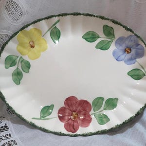 May include: Oval, white ceramic serving platter with a scalloped edge. The platter is decorated with hand-painted flowers in yellow, blue, and burgundy, with green leaves. The rim has a green trim.
