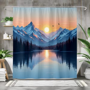 Può includere: Tenda da doccia con un paesaggio montano al tramonto. Le montagne sono blu e il cielo è una sfumatura di arancione e blu. Un lago riflette le montagne e il cielo. Due uccelli volano nel cielo.