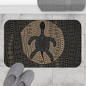 Könnte beinhalten: Rechteckige Badematte mit einem schwarzen Schildkrötendesign und Punktmuster, vor einem beige-schwarzen Hintergrund mit vertikalen Linien und Kreisen. Die Matte liegt auf einem gefliesten Boden, mit grauen Hausschuhen im Vordergrund.