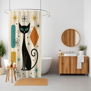 Könnte beinhalten: Cremefarbener Duschvorhang mit Retro-Design. Er zeigt eine schwarze Katze mit türkisfarbenen Augen, geometrische Formen in Türkis, Orange und Gelb sowie Stern- und Atommotive. Der Vorhang hängt in einem Badezimmer.