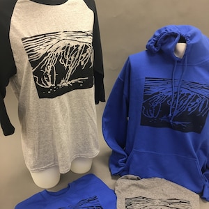 May include: A display of various apparel items, including a gray and black baseball tee, a blue hoodie, and two crew neck shirts. Each item features a black and white graphic design. The items are displayed on mannequins and a flat surface.