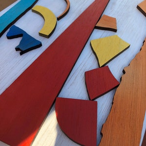 May include: Abstract art wall decor made of wood with geometric shapes in shades of blue, yellow, orange, and red.