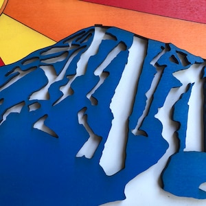 May include: A blue wooden mountain with white cutouts, resembling a ski slope. The mountain is set against a background of orange, red, and yellow.