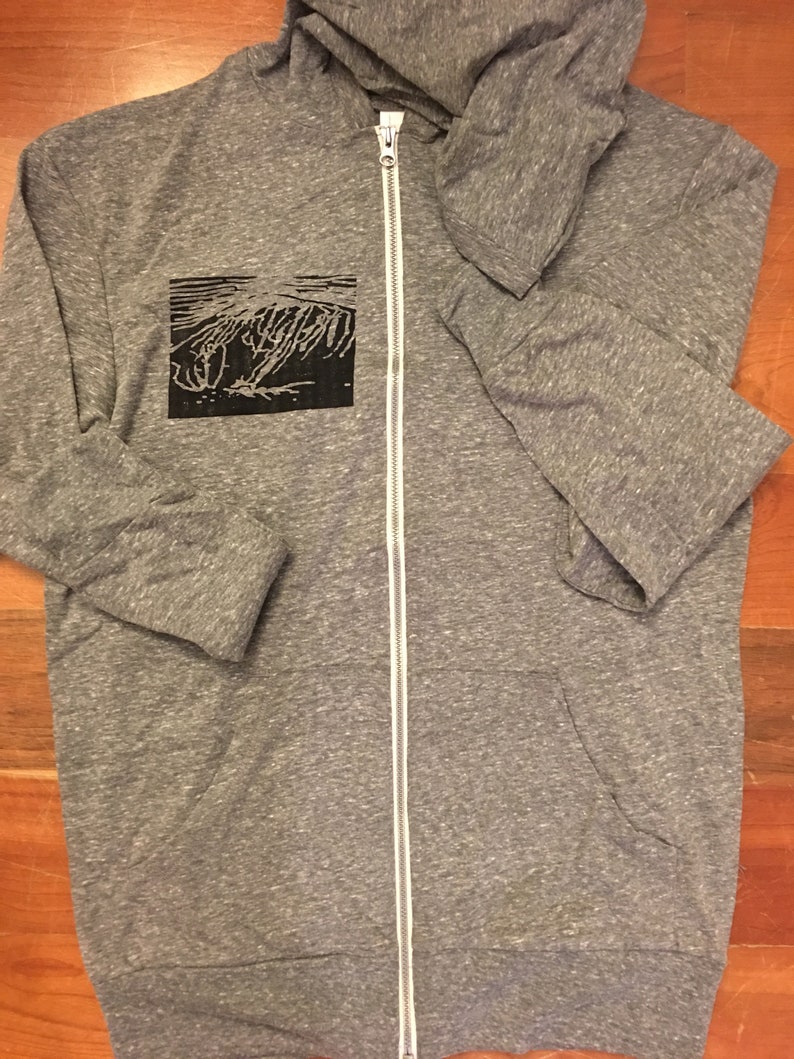 May include: A heather gray zip-up hoodie with a black graphic on the left chest. The hoodie has a white zipper and a hood. The graphic appears to be an abstract design. The hoodie is made of a soft, comfortable material.