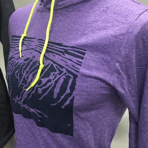 May include: A purple hoodie with a graphic design on the front. The hoodie has a drawstring with neon yellow cords and a hood. The graphic is a dark blue abstract design. The hoodie is displayed on a mannequin.