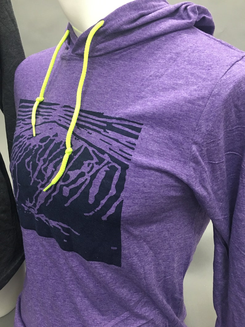 May include: A purple hoodie with a graphic design on the front. The hoodie has a drawstring with neon yellow cords and a hood. The graphic is a dark blue abstract design. The hoodie is displayed on a mannequin.