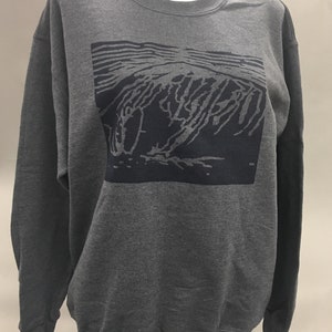May include: A dark gray sweatshirt with a crew neck and long sleeves. The front features a rectangular graphic in a darker shade of gray, depicting an abstract design. The sweatshirt is displayed on a mannequin.