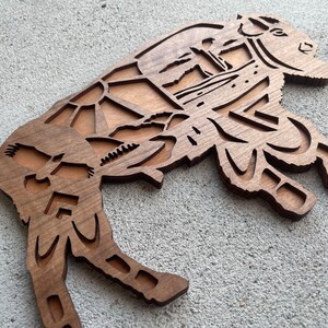 May include: A wooden cutout of a bison with a detailed design of a sunset and birds in flight. The bison is brown and the design is in a lighter wood tone.