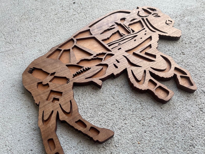 May include: A wooden cutout of a bison with a detailed design of a sunset and birds in flight. The bison is brown and the design is in a lighter wood tone.