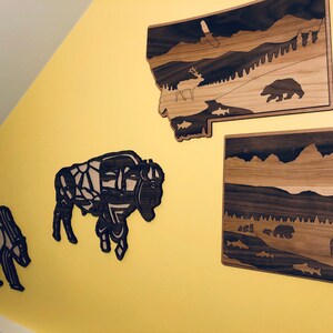May include: Four wooden wall decorations featuring a bison, a bear, a deer, and a mountain landscape. The decorations are made of dark wood with a light wood inlay.