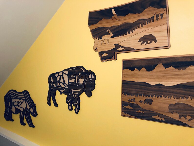 May include: Four wooden wall decorations featuring a bison, a bear, a deer, and a mountain landscape. The decorations are made of dark wood with a light wood inlay.