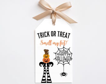 Może przedstawiać: Biała prostokątna zawieszka prezentowa z beżową kokardką na górze. Tekst brzmi TRICK OR TREAT oraz Smell my feet! w kolorze czarnym i pomarańczowym. Zawiera brązowego psa na dwóch pomarańczowych dyniach, czarno-białe pasiaste nogi i pajęczynę.