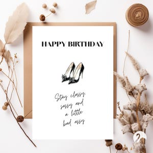 Könnte beinhalten: Eine weiße Geburtstagskarte mit den Worten "HAPPY BIRTHDAY" in Schwarz. Darunter eine Illustration von schwarzen High Heels mit Schleifen. Die Karte enthält auch den Text "Stay classy, sassy and a little bad assy."