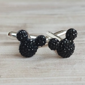 May include: A pair of black cufflinks featuring a Mickey Mouse head design. The cufflinks are made of metal and have a silver finish.