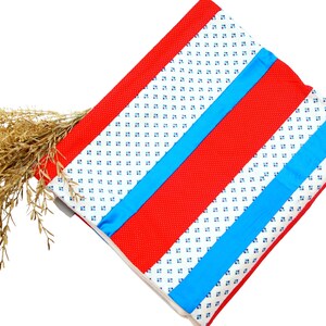 May include: A folded quilt with a red border and stripes. The quilt features red, white, and blue colors. The white sections have a small blue floral pattern. A bundle of dried, golden-brown grass is placed on the quilt.