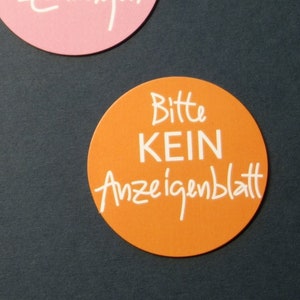 Könnte beinhalten: Drei runde Aufkleber in Rot, Rosa und Orange. Der rote Aufkleber trägt den weißen Text "Bitte KEINE Werbung!". Der rosa Aufkleber trägt den weißen Text "...und kostenlose Zeitungen". Der orangefarbene Aufkleber trägt den weißen Text "Bitte KEIN Anzeigenblatt".