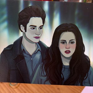 May include: A rectangular print featuring a stylised digital illustration of two figures with pale skin and dark hair. The figure on the left wears a dark jacket over a blue shirt, while the figure on the right has long wavy dark hair and a blue top.