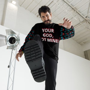 May include: A black Christmas sweater with a red and green holly pattern on the sleeves. The sweater has the text "YOUR GOD, NOT MINE!" printed on the front.