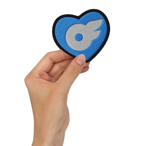 May include: A blue heart-shaped patch with a white stylized bird logo. The patch is embroidered and has a black border.