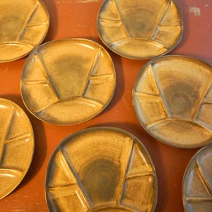 May include: Six brown ceramic divided plates with a speckled glaze. The plates are designed for serving fondue or other multi-course meals.