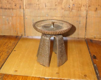 May include: A rustic iron candle holder with a round top and three legs. The holder has a textured surface and is a dark brown color.
