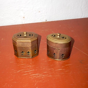 Peut inclure: Deux récipients en laiton antique avec des motifs ornés et des couvercles. Les récipients présentent un motif décoratif de découpes de fleurs de lys.