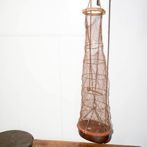 May include: A vintage, hanging wire mesh basket with a wooden rim and base, suspended from a door handle. The basket is brown and has a cylindrical shape, suitable for storage or display.