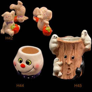 May include: A collection of Halloween-themed ceramic figurines. Includes ghosts holding pumpkins, a smiling face planter, and a tree stump planter with ghosts and a black cat. The figurines are painted in pastel colors.