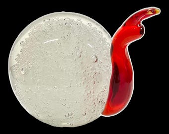 May include: A clear glass sculpture with a spherical body filled with bubbles and a curved, red accent. The red accent has a yellow tip. The sculpture is set against a black background.