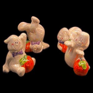 May include: Three iridescent ceramic ghost figurines, each featuring a glossy finish, a purple bowtie, and a smiling orange pumpkin. The ghosts are depicted in various poses, including sitting and reclining, with hand-painted facial features.