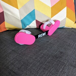 May include: Pink foot and ankle support with adjustable straps and the word "REMI" printed on the black connecting strap.