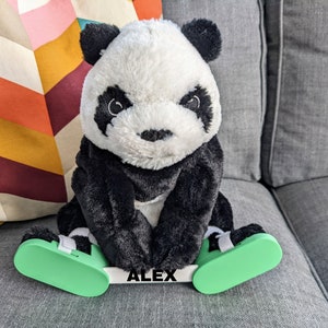 May include: A black and white panda plush toy wearing green and white shoes with the name "ALEX" printed on the front.
