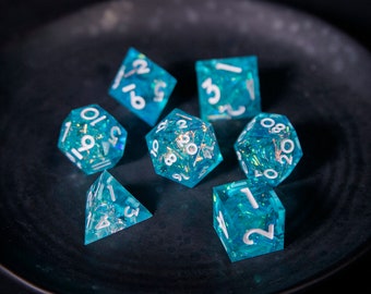 May include: A set of seven polyhedral dice in various shapes, each with a translucent teal color and white numbering. The dice are scattered on a dark, textured surface, creating a visually appealing arrangement for tabletop gaming.