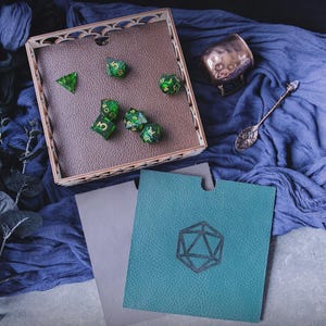 May include: A wooden dice tray with a green and gold dice set. The tray has a decorative design and is sitting on a blue fabric surface.