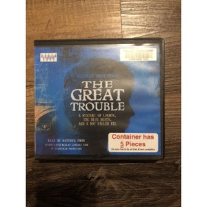 May include: A blue and white DVD case with the title "The Great Trouble" by Deborah Hopkinson. The case has a barcode and the text "Container has 5 Pieces. Do not check In or Out if not complete."