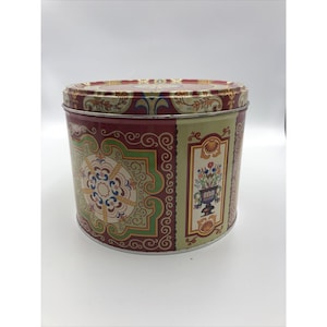 May include: A vintage round tin container with a red, green, and gold floral design. The tin has a decorative border with a floral pattern.