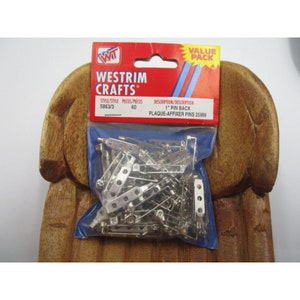 May include: A pack of 60 silver-coloured 25mm pin backs, also known as plaque-affixer pins, for crafts. The package is labelled "Westrim Crafts" and includes product information. The pins are in a clear plastic bag.