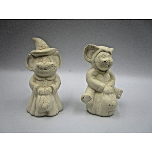 以下が含まれることがあります： ハロウィーンの衣装を着た白い陶器製のネズミの置物2体。1匹は魔女の帽子をかぶり、カボチャを持っています。もう1匹はフード付きのマントを着て、袋を持っています。