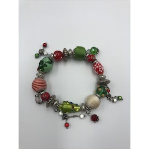 Könnte beinhalten: Ein Armband im Weihnachtsdesign mit roten, grünen und weißen Perlen, darunter ein kleiner Weihnachtsbaum-Anhänger.