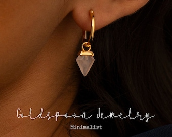 May include: Gold hoop earrings with a pink crystal pendant. The earrings are minimalist and delicate.