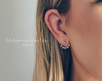 May include: Close-up of a woman's ear adorned with two pieces of jewelry. The first is a small stud earring. The second is a silver ear jacket with a series of small, round, clear stones. The text "Goldspoon Jewelry Minimalist" is visible.