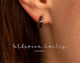 May include: A black hoop earring with a small diamond accent. The earring is worn in a person's ear.