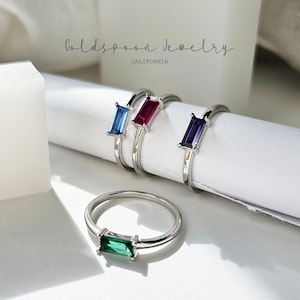 May include: Four silver rings with different colored rectangular gemstones. The rings are arranged on a white surface. The text "Goldspoon Jewelry CALIFORNIA" is visible at the top of the image.