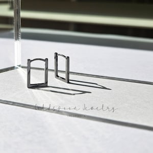 May include: A pair of black square hoop earrings. The earrings are made of metal and have a simple, minimalist design.