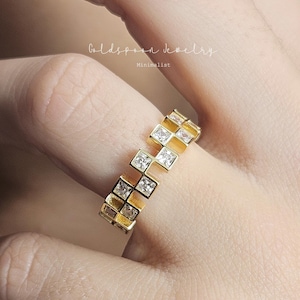 May include: Gold ring with a minimalist design featuring a series of square-shaped stones set in a gold band.