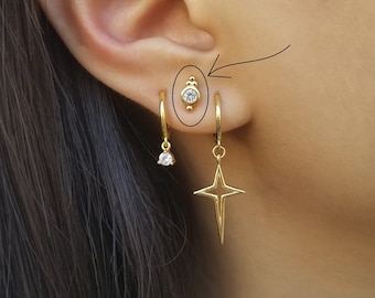Puede incluir: Aretes de aro de oro con un dije de estrella colgante y un pequeño arete de cristal transparente en el cartílago de la oreja.